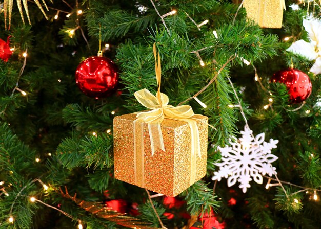 Gold glitter square gift box with other colorful Christmas ornaments on a sparkling Christmas Tree