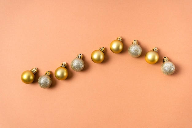 Sfere scintillanti d'oro su un albero di natale sono disposte in fila su uno sfondo beige. decorazioni natalizie
