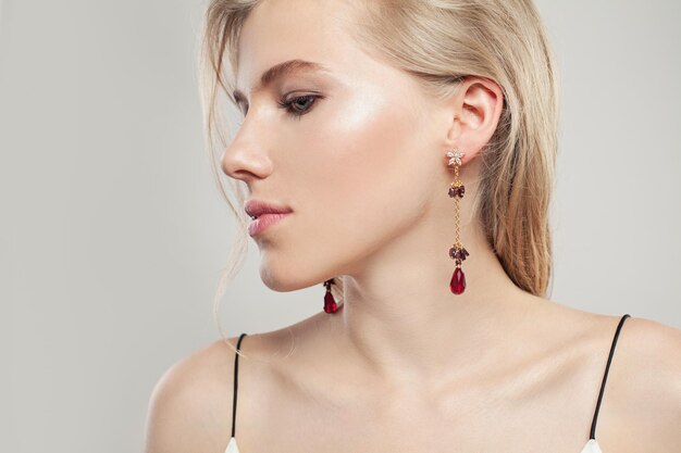 Gold jewelry model Beautiful woman with fashion golden earrings with red garnet on white background