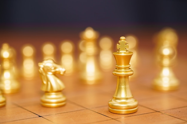 Pezzo degli scacchi re d'oro e vari pezzi degli scacchi stanno sulla scacchiera in legno, concetto di gioco di strategia di leadership