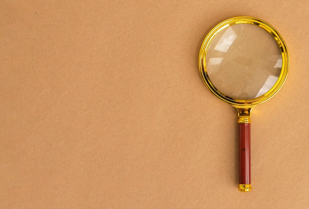 Gold magnifying lens over brown carton background. Search tool with copy space for text.