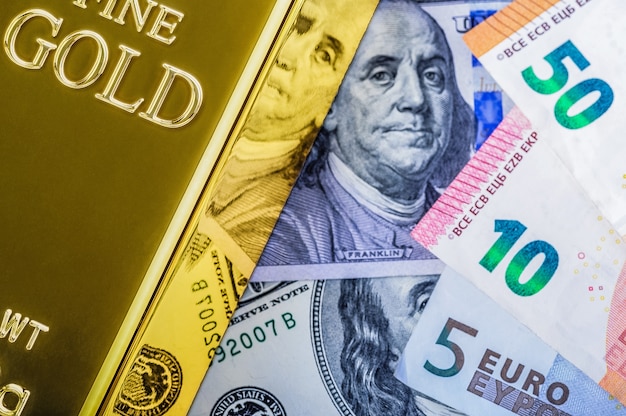 Lingotto di lingotti di metallo oro sullo sfondo del dollaro e fatture in euro.