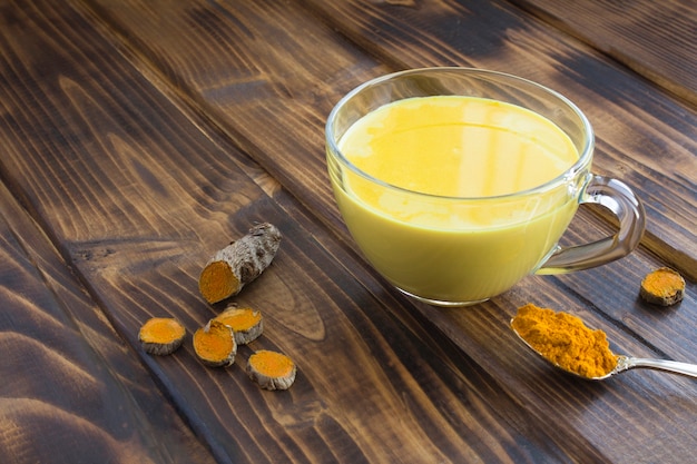 Gold milk with turmeric in the glass cup on the wooden background