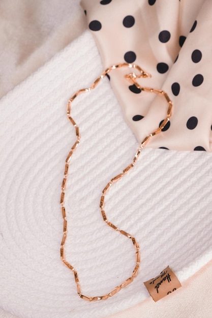 A gold necklace with black and white polka dots sits on a white cloth.