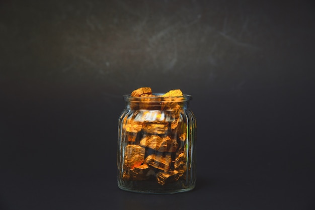 Gold nuggets, gold ore and glass jar in dark room.