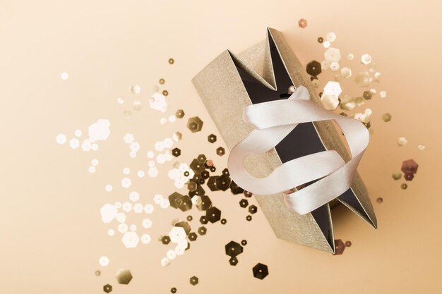 Золотая бумажная сумка для покупок и модные шестиугольные блестки на бежевом фоне Концепция праздничной распродажи в монохромных тонах