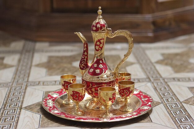 A gold plate with a red and white teapot and cups on it.