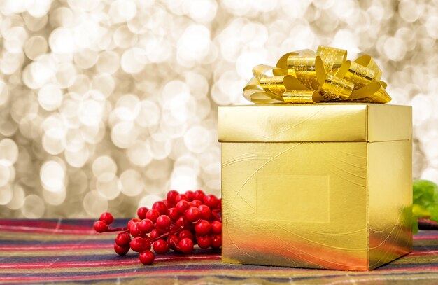 Gold present box with ribbon on table with sparkling gold bokeh light background