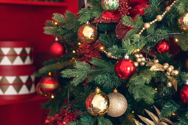 Gold and red Christmas toys, balls, garlands on a spruce branch on dark red background.