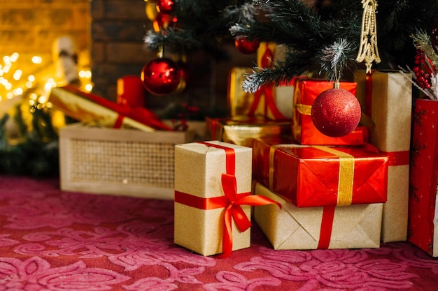 Gold and red gift boxes are under the Christmas tree near the fireplace