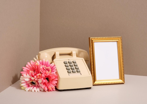 Gold retro style photo frame and beige phone with gray buttons spring flowers