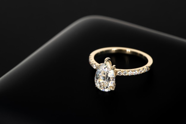 A gold ring with a diamond on it sits on a black background.