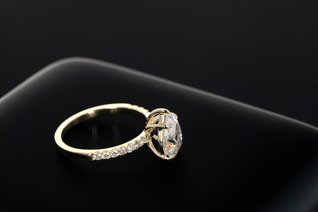 A gold ring with a diamond on it sits on a black background.