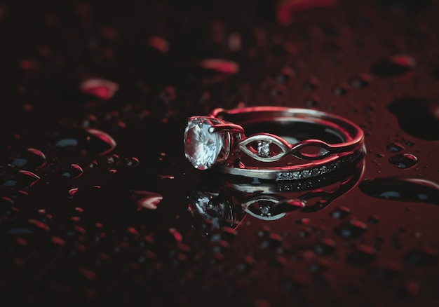 Gold rings with a diamond in bluered neon light on a dark with drops of water