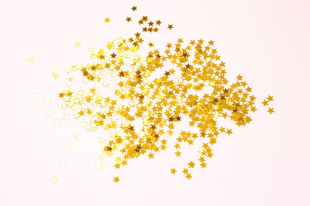 Photo gold sequins in the shape of stars shimmer on a pink background. backgrounds with copyspace for a holiday, party decoration, christmas and new year, birthday and anniversary. gradient and texture