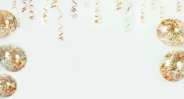 Gold serpentine holiday decoration and balloons with colorful confetti on light background