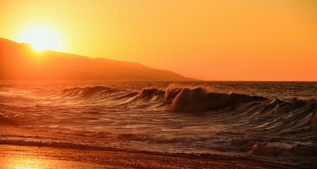 滑らかな波と夕日の空の抽象的な背景黄金の太陽と金色の空と海水の熱帯のビーチ
