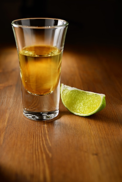 Gold tequila shot with lime on the wooden bar