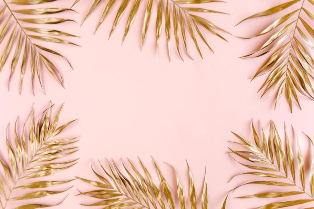 Gold tropical palm leaves on pink background flat lay top view minimal concept