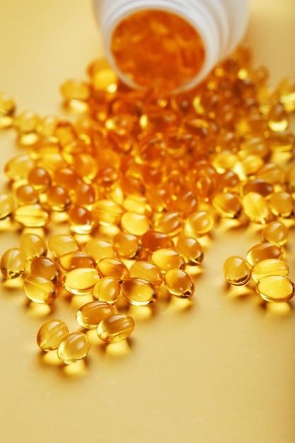 Gold Vitamin D3 capsules poured out of a jar on a yellow background with free space