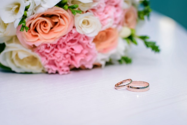 Gold wedding rings and bridal bouquet on white surface