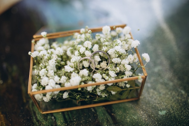 Fedi in oro in una scatola di vetro con fiori bianchi