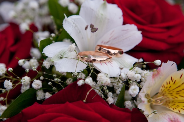 Gold wedding rings of the groom and the bride lie on a bouquet of the bride