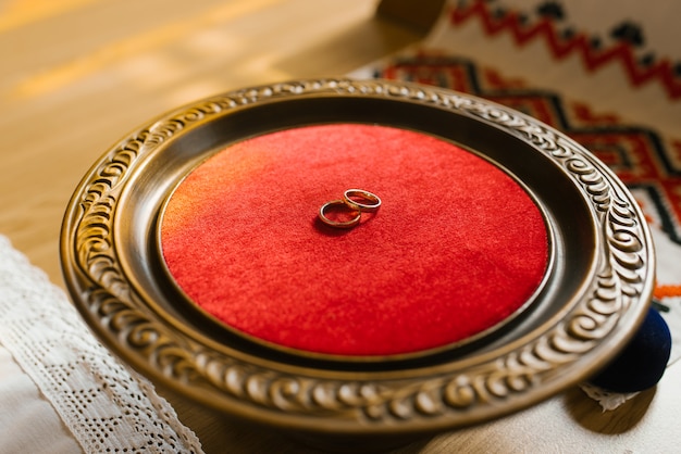 Gold wedding rings lie on a wooden plate with red velvet