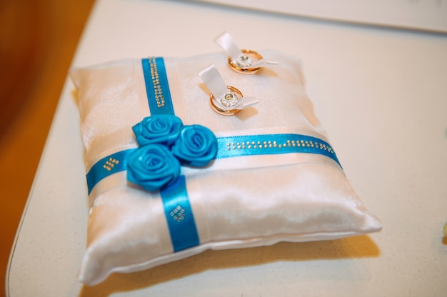 Gold wedding rings on a white cushion decorated with ribbons and flowers, close-up. Wedding theme, accessories for newlyweds.