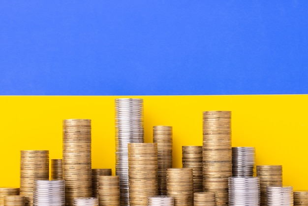 Фото Золотые и серебряные стопки денег перед флагом украины