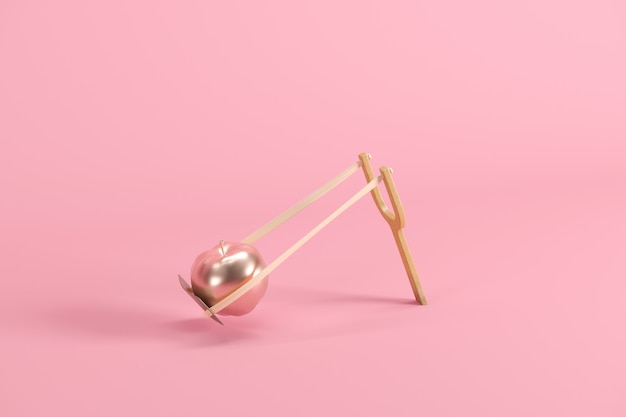 Golden apple in a slingshot on pink background