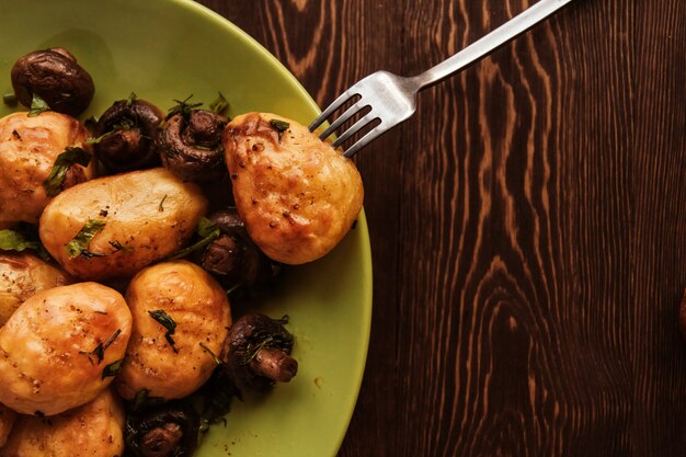 Golden baked potatoes and fried champignons on a green plate on a wooden table copy space. Potatoes with mushrooms.