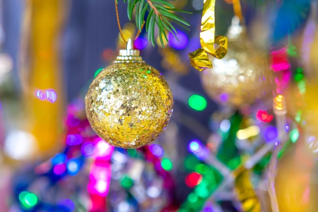 Golden ball on a spruce branch decorated for christmas and new year among serpentine and garlands with lights closeup