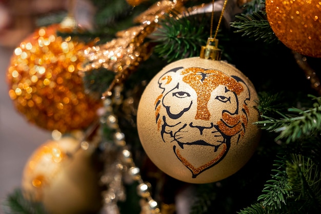 Golden ball with tiger head ornament on christmas tree with\
bokeh lights on background. close-up christmas decorations. merry\
christmas and happy new year 2022 greeting card.