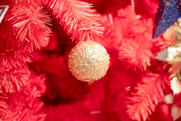 Golden baubles glowing and hanging on decorated red christmas tree