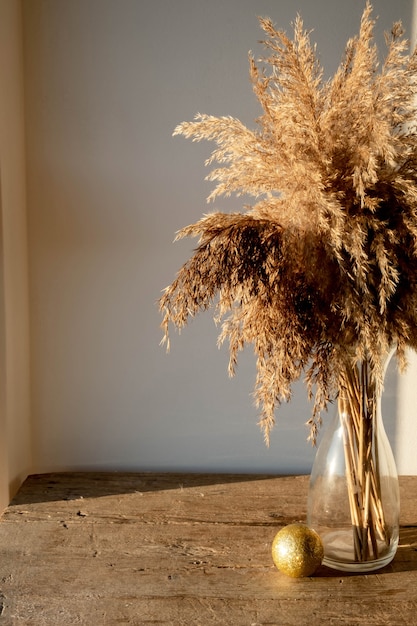 Photo golden beige pampas grass stands in a glass vase on a wooden background in the rays