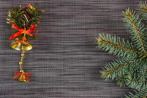 Золотой колокольчик, ветка елки на сером новогоднем фоне с медным пространством. Рождественские украшения.