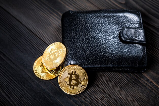 Golden bitcoin and black purse on wood background