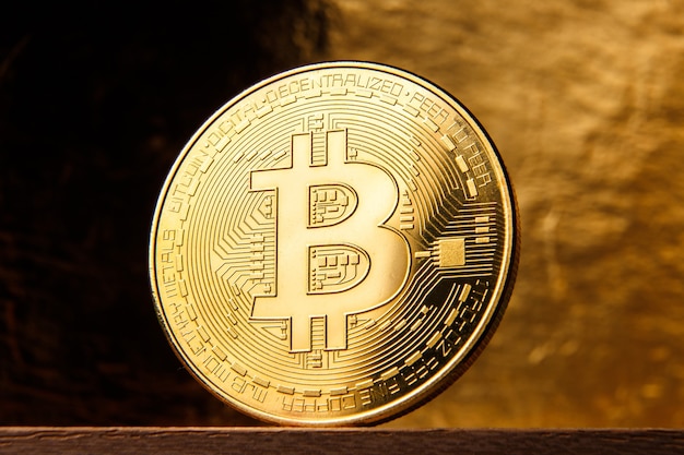 Golden bitcoin coin close up on black and gold gradient background.