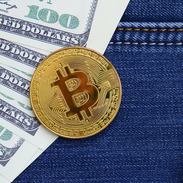 Golden Bitcoin and dollar bills lies on a blue jeans fabric