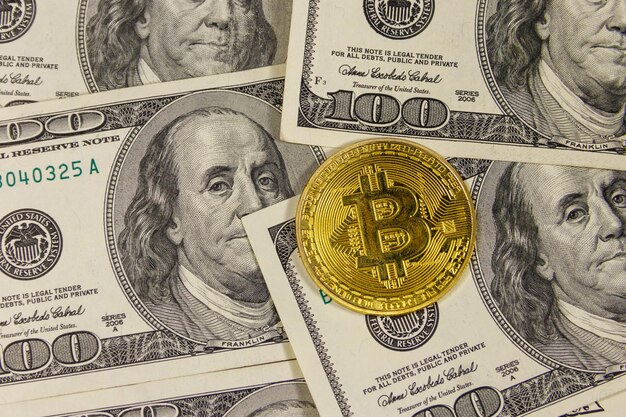 Golden bitcoin on hundred dollar bills background