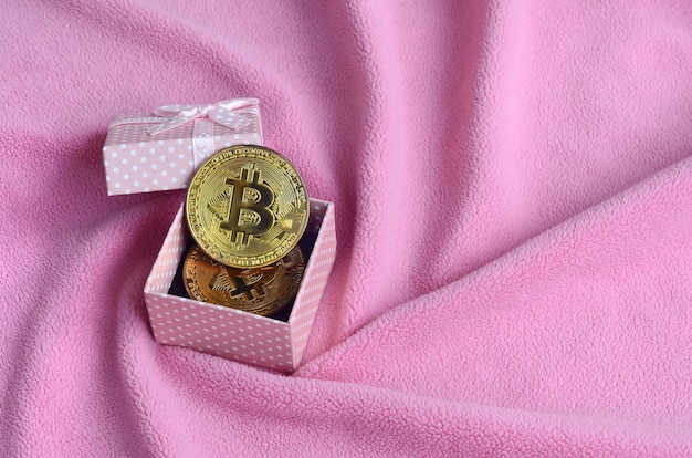 The golden bitcoin lies in a small pink gift box with a small bow 