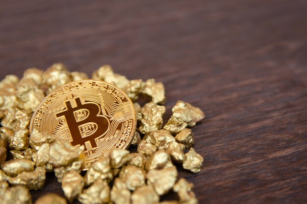 Golden bitcoin on mound of gold nugget on dark wood