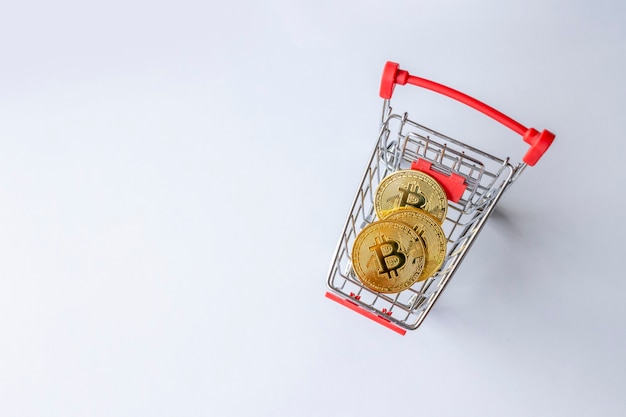 Golden bitcoin in shopping cart on white table background. top view