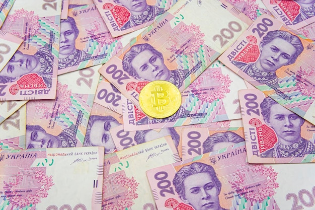 Golden bitcoin on two hundred ukrainian hryvnia bills background