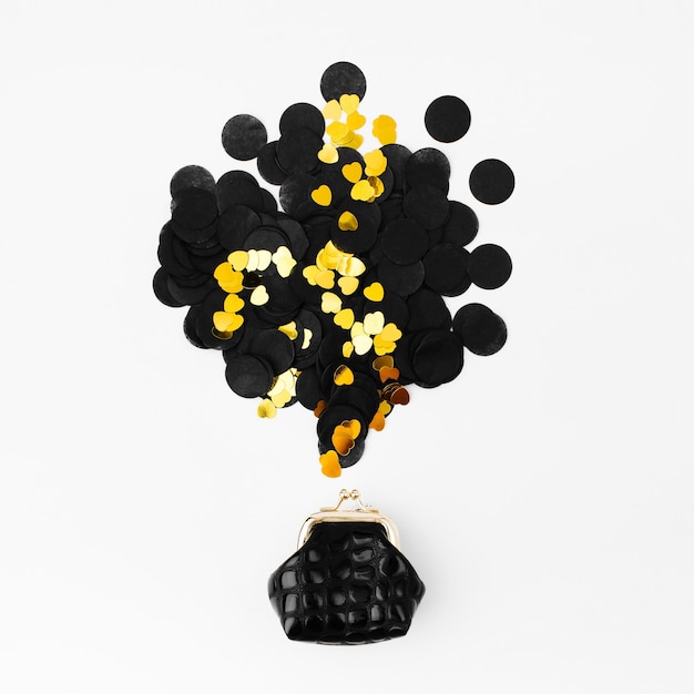 Golden and black confetti falling out of  purse on white background