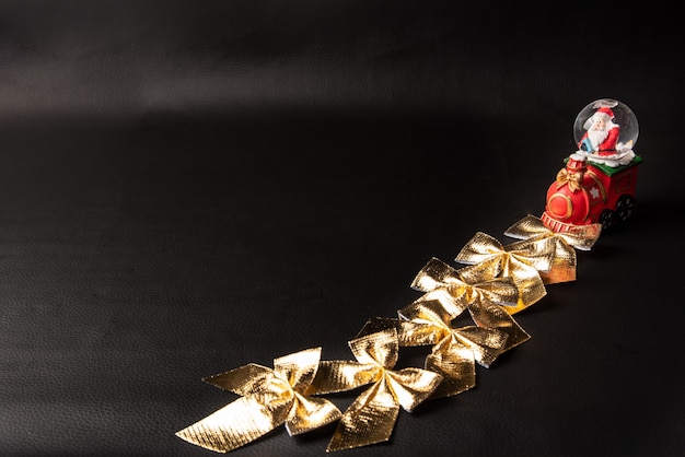 Golden bows, pile of beautiful golden bows and globe with Santa Claus on black background, Low Key portrait, selective focus.