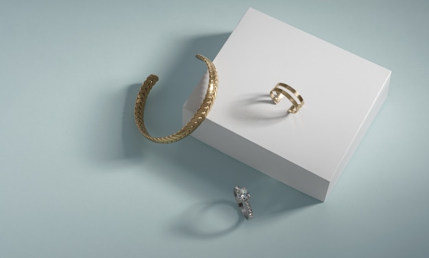 Photo golden bracelet and rings on white box on blue background with copy space