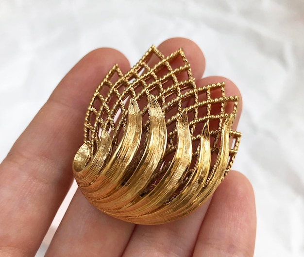 golden brooch in hand on white background close up
