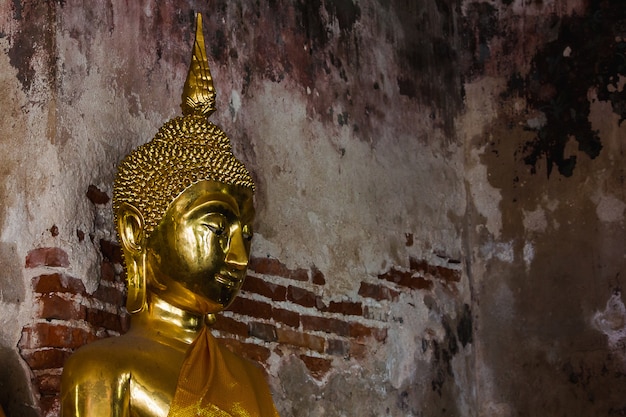 Buddha d'oro accanto a vecchie mura nei templi thailandesi